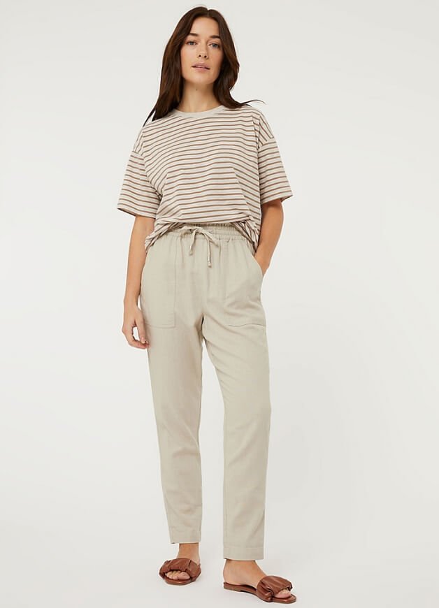 A woman posing in a beige striped t-shirt and stone trousers